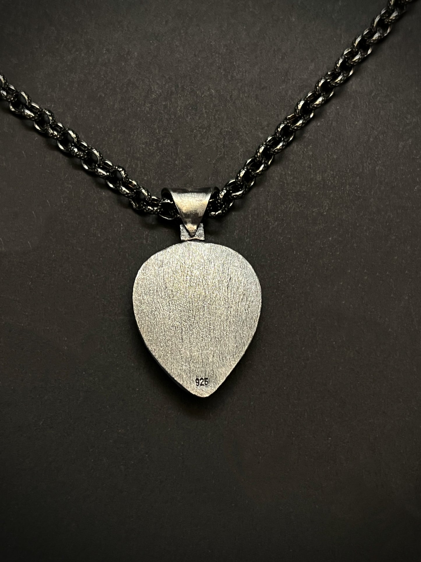 Silver pendant on a black chain against a dark background