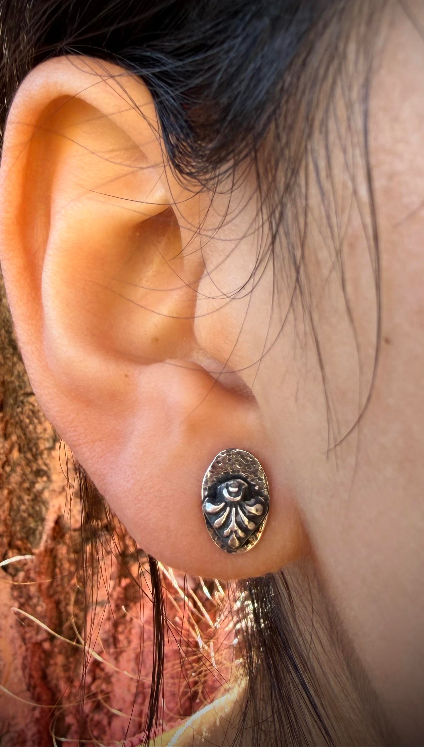 Close-up of an ear wearing a silver earring with a natural background