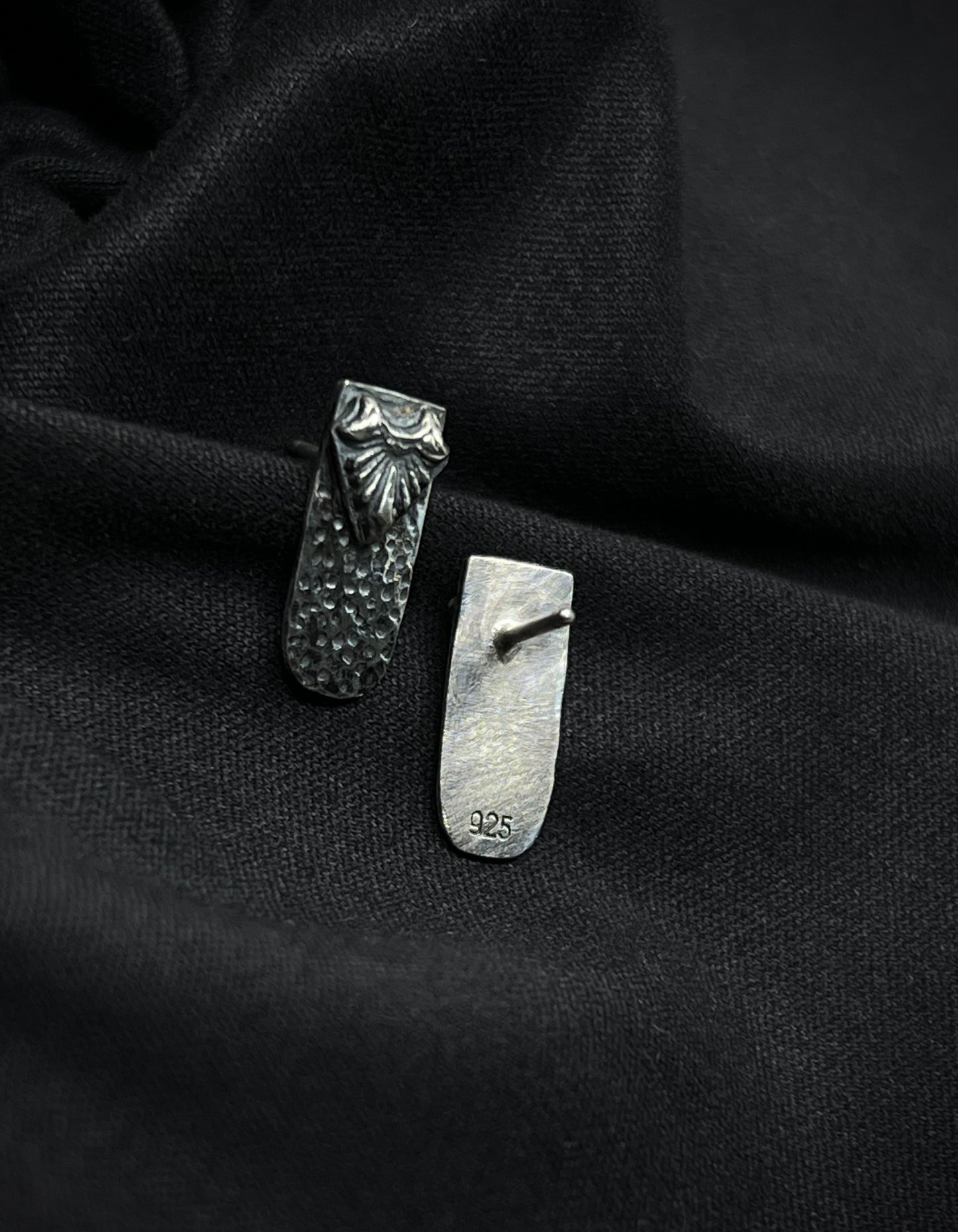 Back and front view of Ashborn Root silver studs on black fabric, showing the 925 sterling silver hallmark and the high-contrast radiating design with hammered textures.