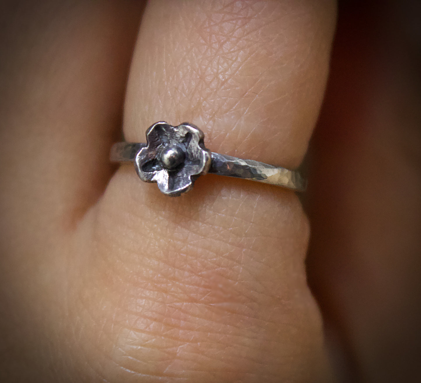 Silver flower-shaped ring on a finger with a blurred background