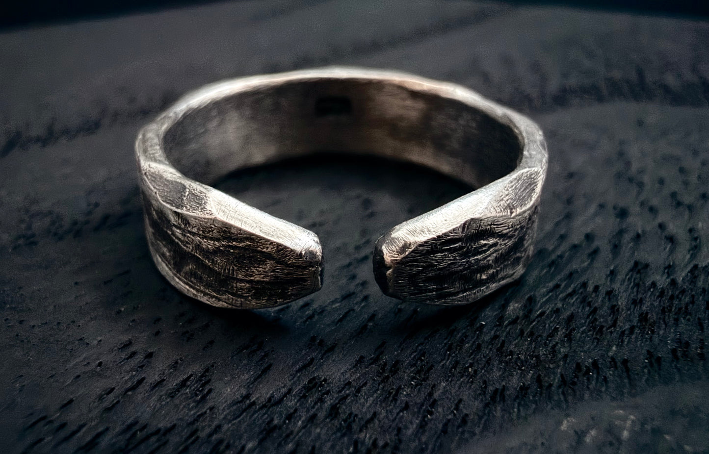 Silver ring with a textured design on a dark wooden surface