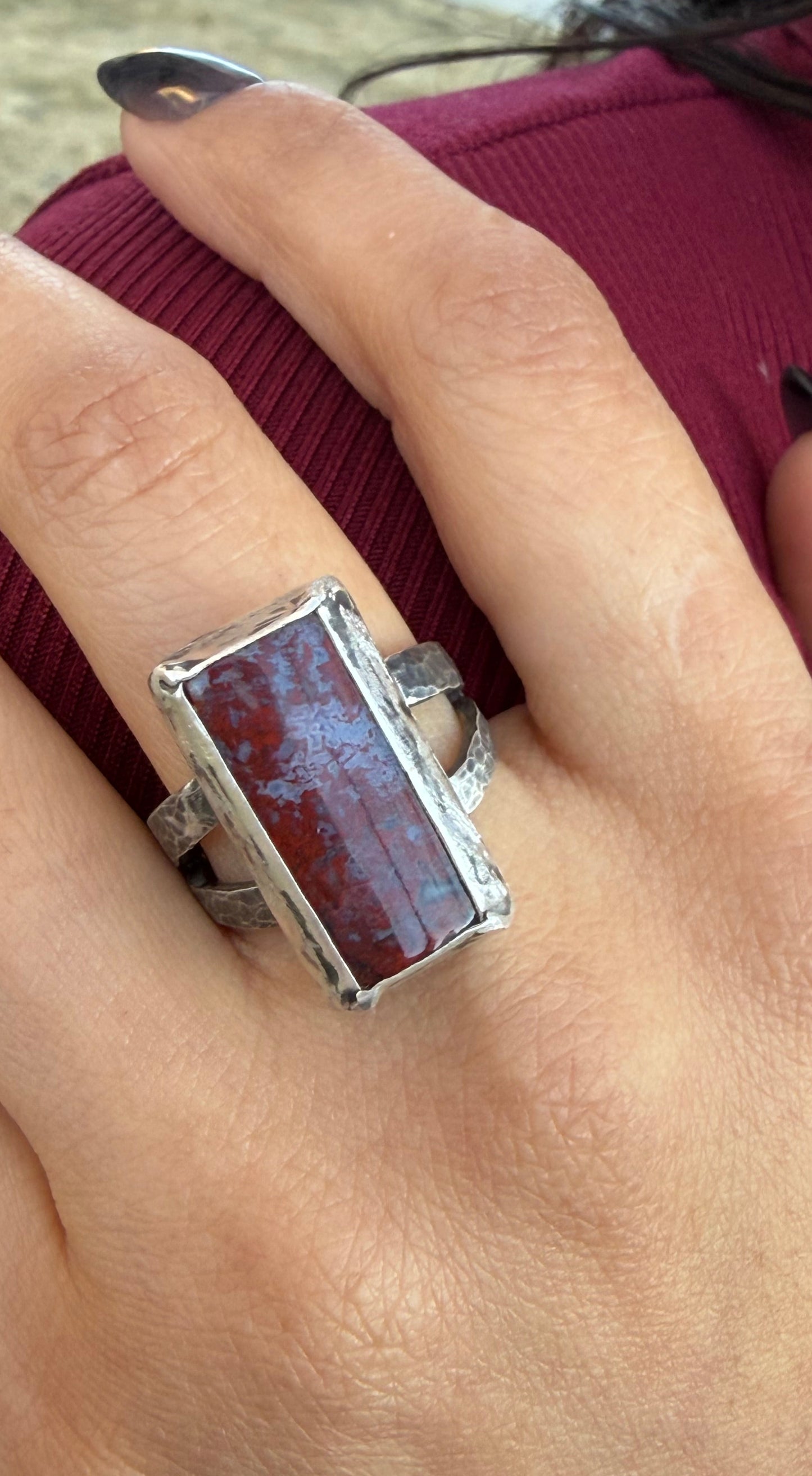 Hand wearing a silver ring with a rectangular stone, blurred background