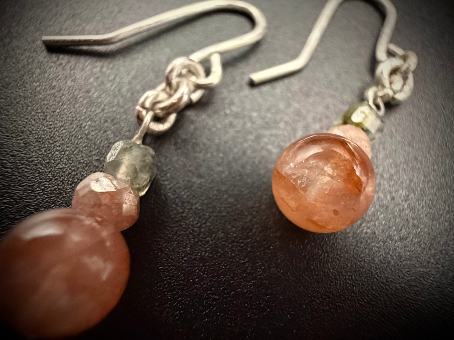 Close-up of Dahlia Drops earrings on a dark surface, showing the detailed textures of the Red Agate, Peach Moonstone, and light green Prehnite beads.