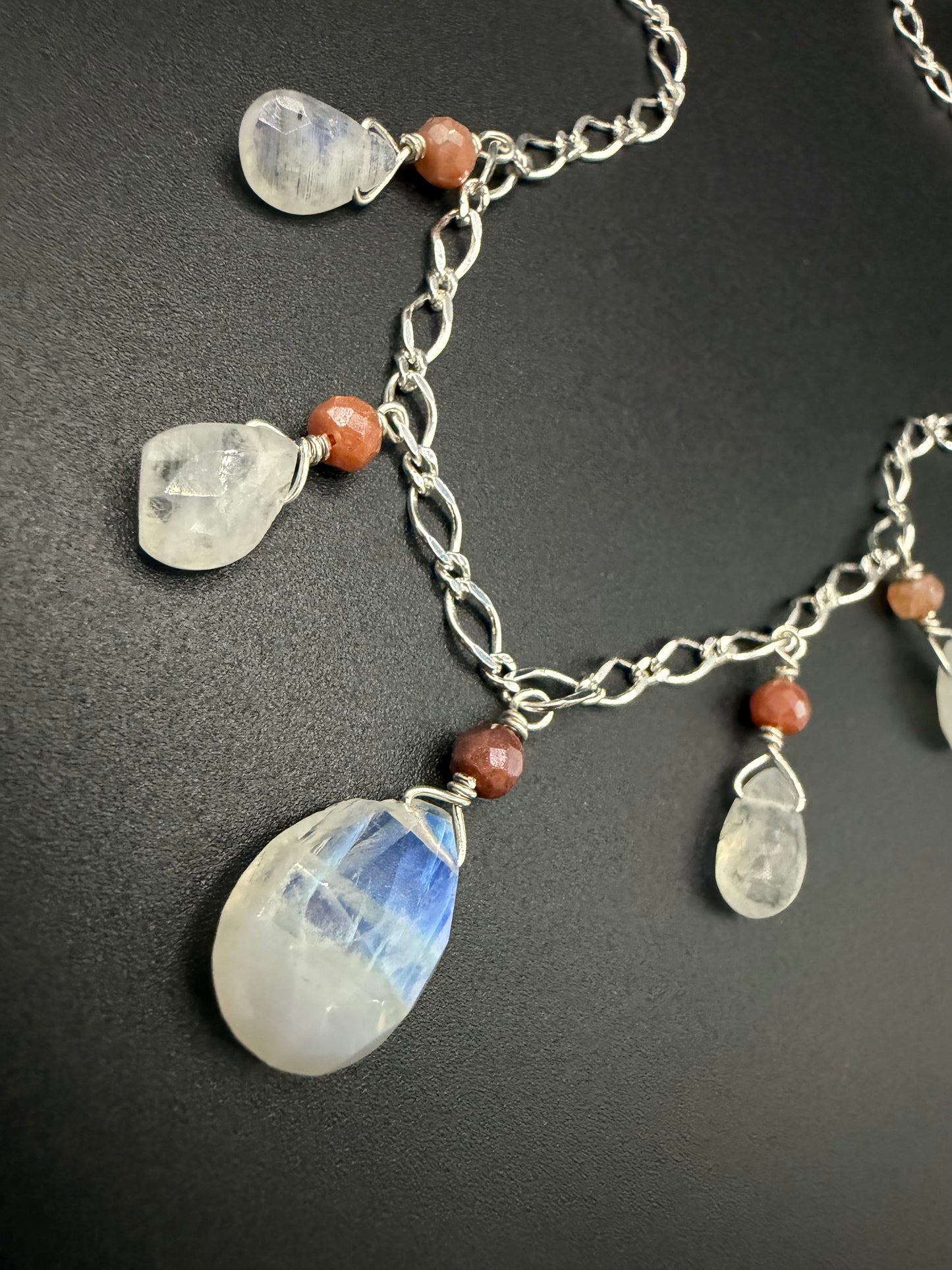 Handcrafted sterling silver necklace featuring large teardrop rainbow moonstones with blue flashes and round peach moonstone beads on a textured silver chain.