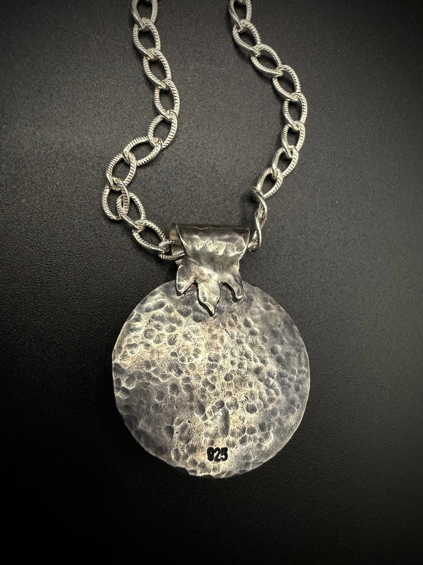 The reverse side of a handcrafted sterling silver pendant, showcasing a clean, heavily hammered metal texture, a secure fine silver bezel setting, a 925 silver hallmark stamp near the bottom, and a stylized textured leaf bail on a silver chain.