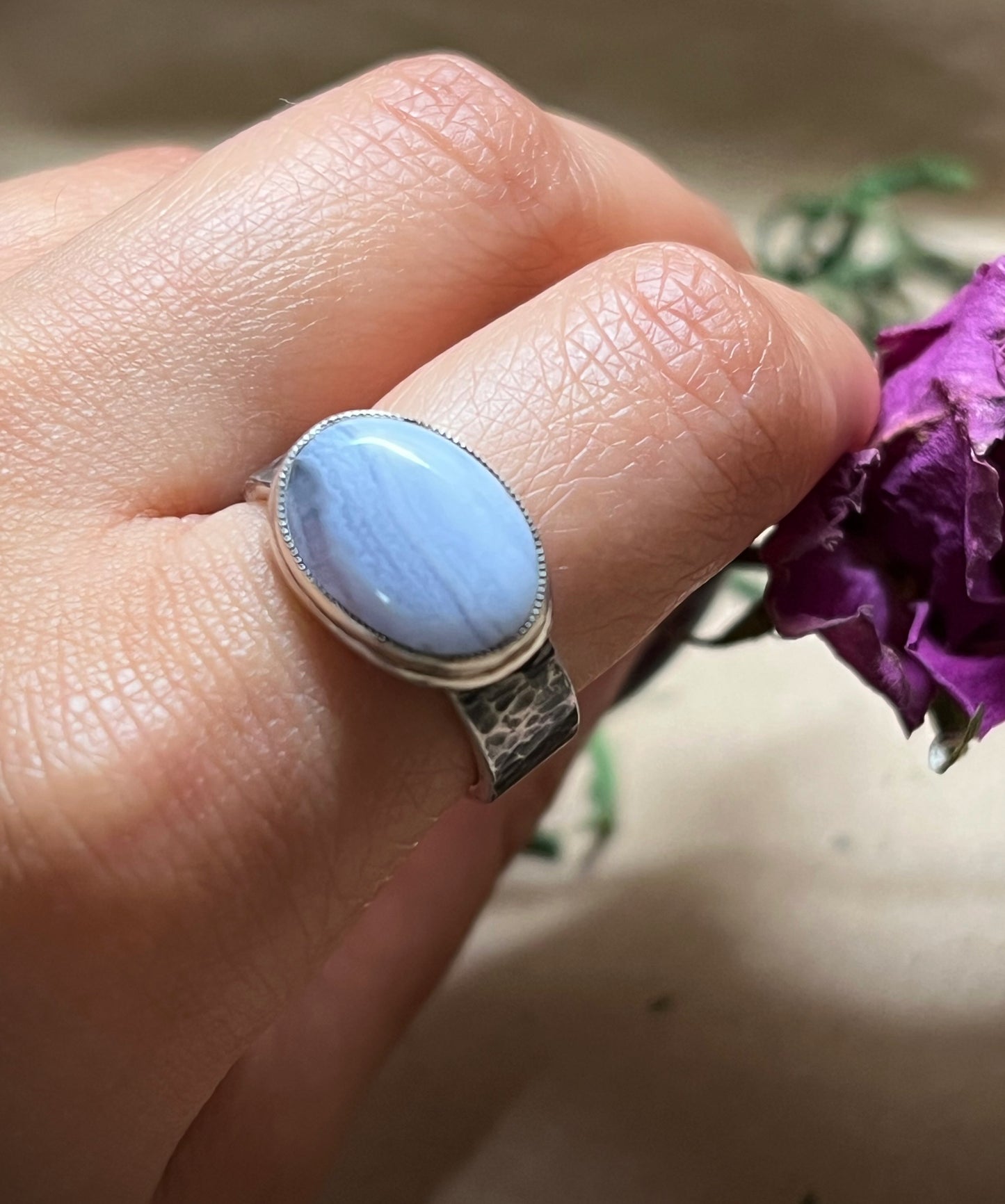 Hand wearing a ring with a blue stone against a blurred background