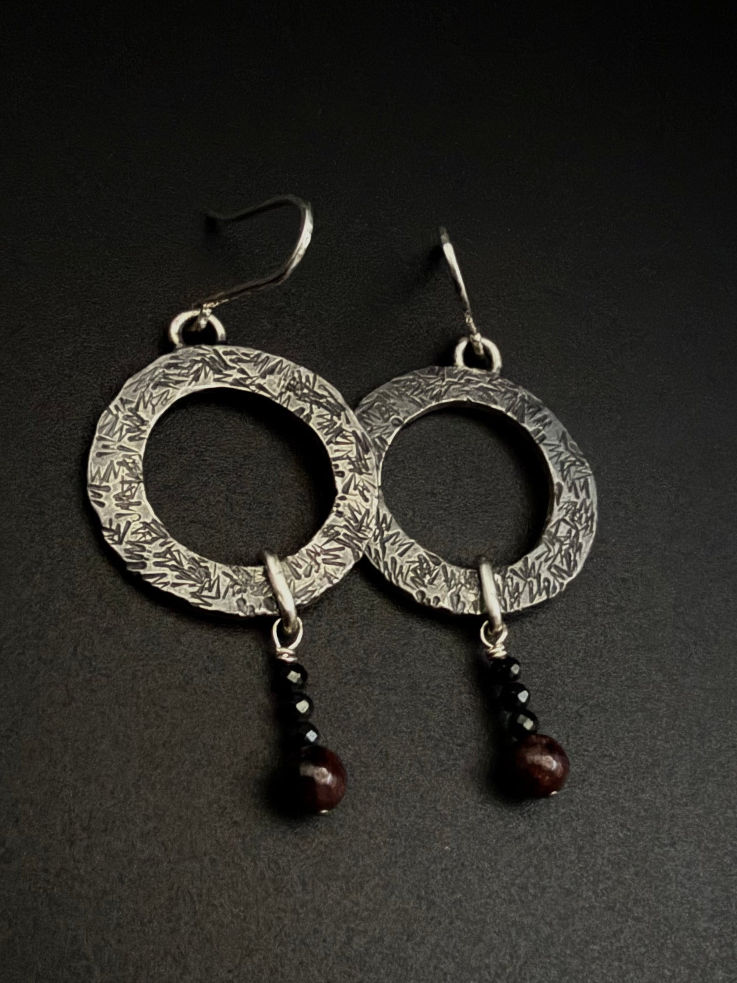 Hoop textured earrings with dangaling beeds on a black background.