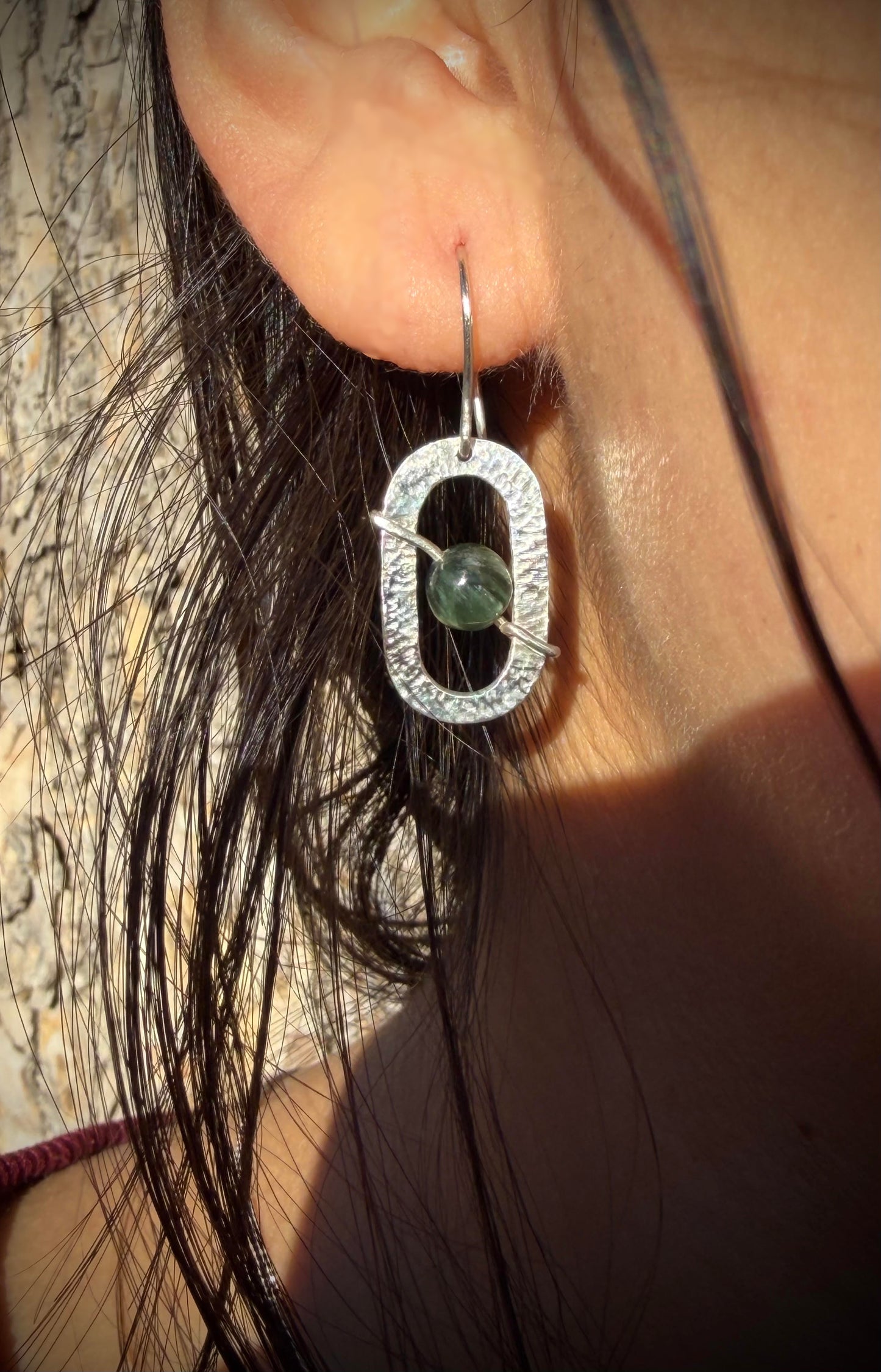 Silver earring with a green gemstone worn by a person with dark hair.