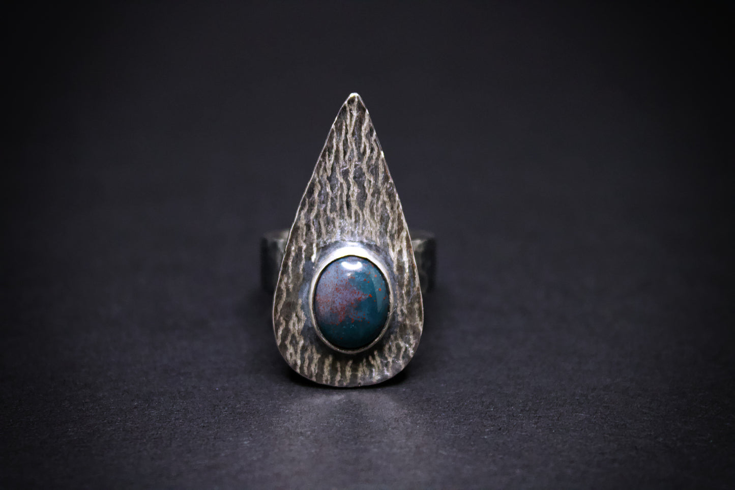 Silver ring with a textured band. green and red blood stone on a black background