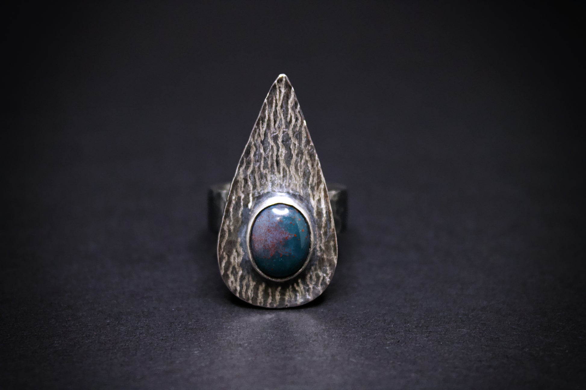 Silver ring with a textured band. green and red blood stone on a black background