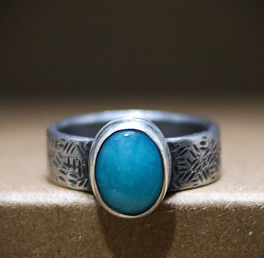 Silver ring with a turquoise stone on a textured surface