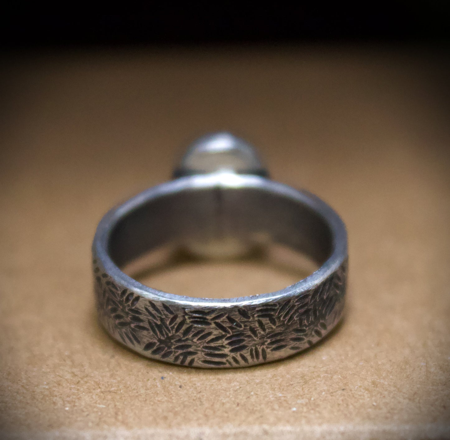 Silver ring with textured design on a brown surface