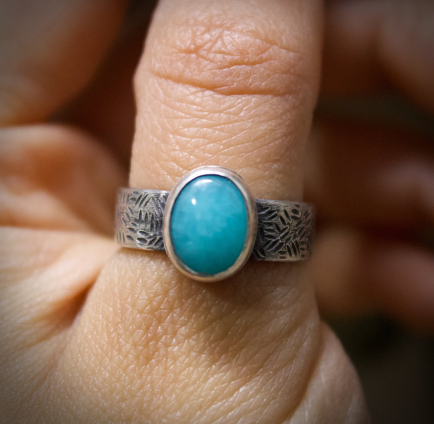 Silver ring with a turquoise stone on a finger against a blurred background