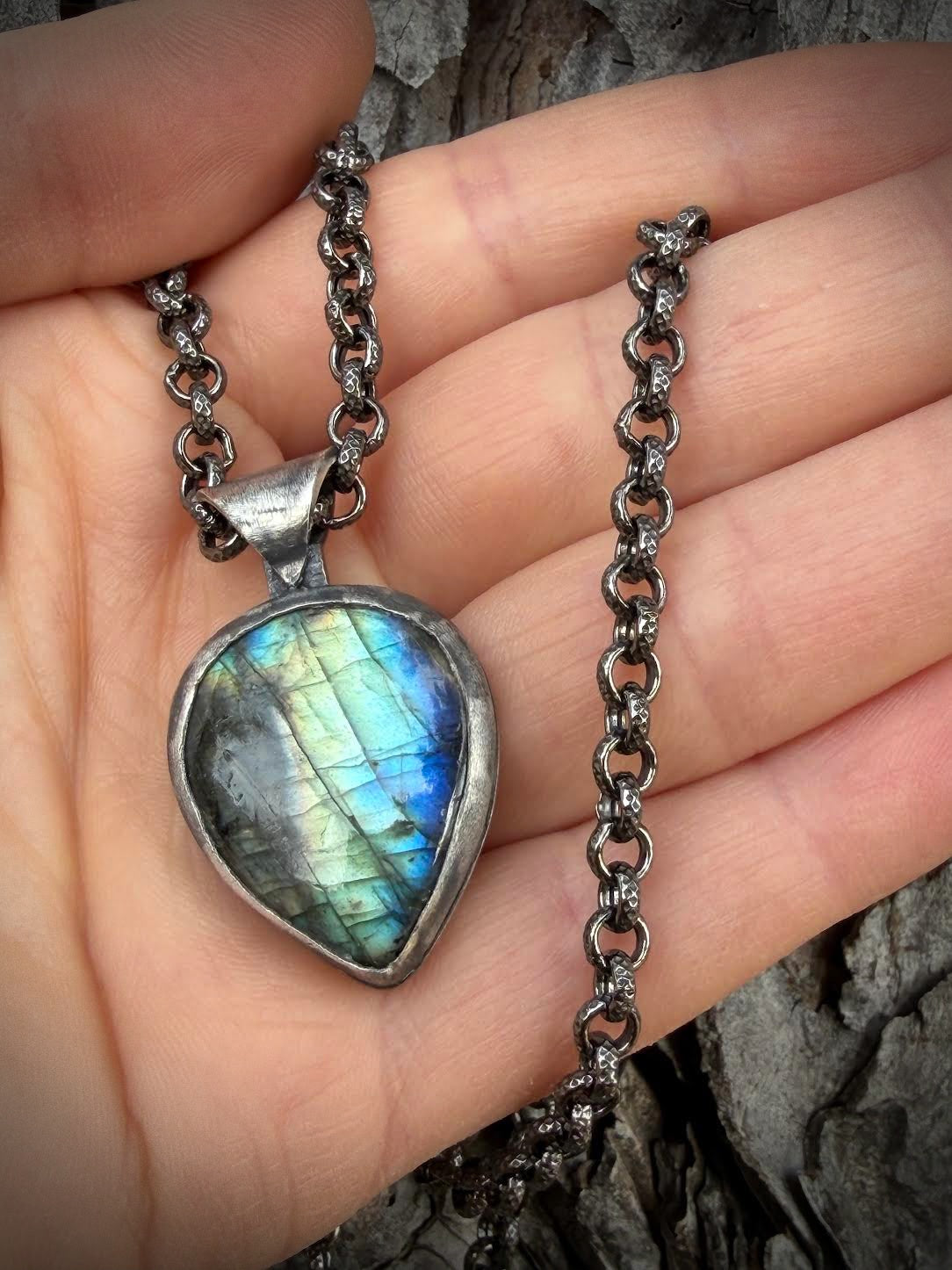 Necklace with a Labradorite pendant held in a hand against a wooden background