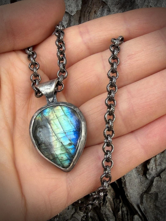 Necklace with a Labradorite pendant held in a hand against a wooden background