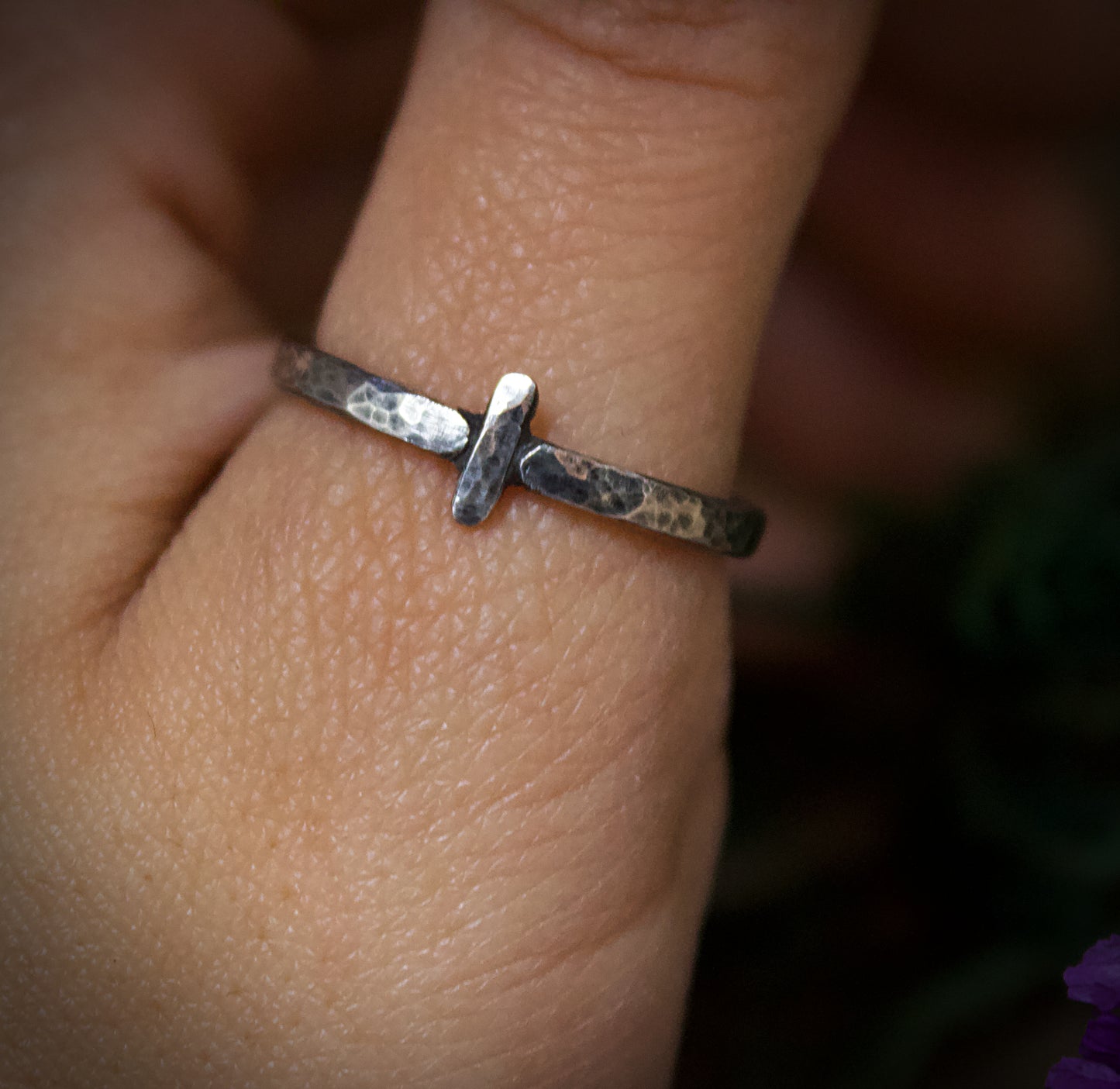 Silver ring with a unique design on a person's finger against a blurred background