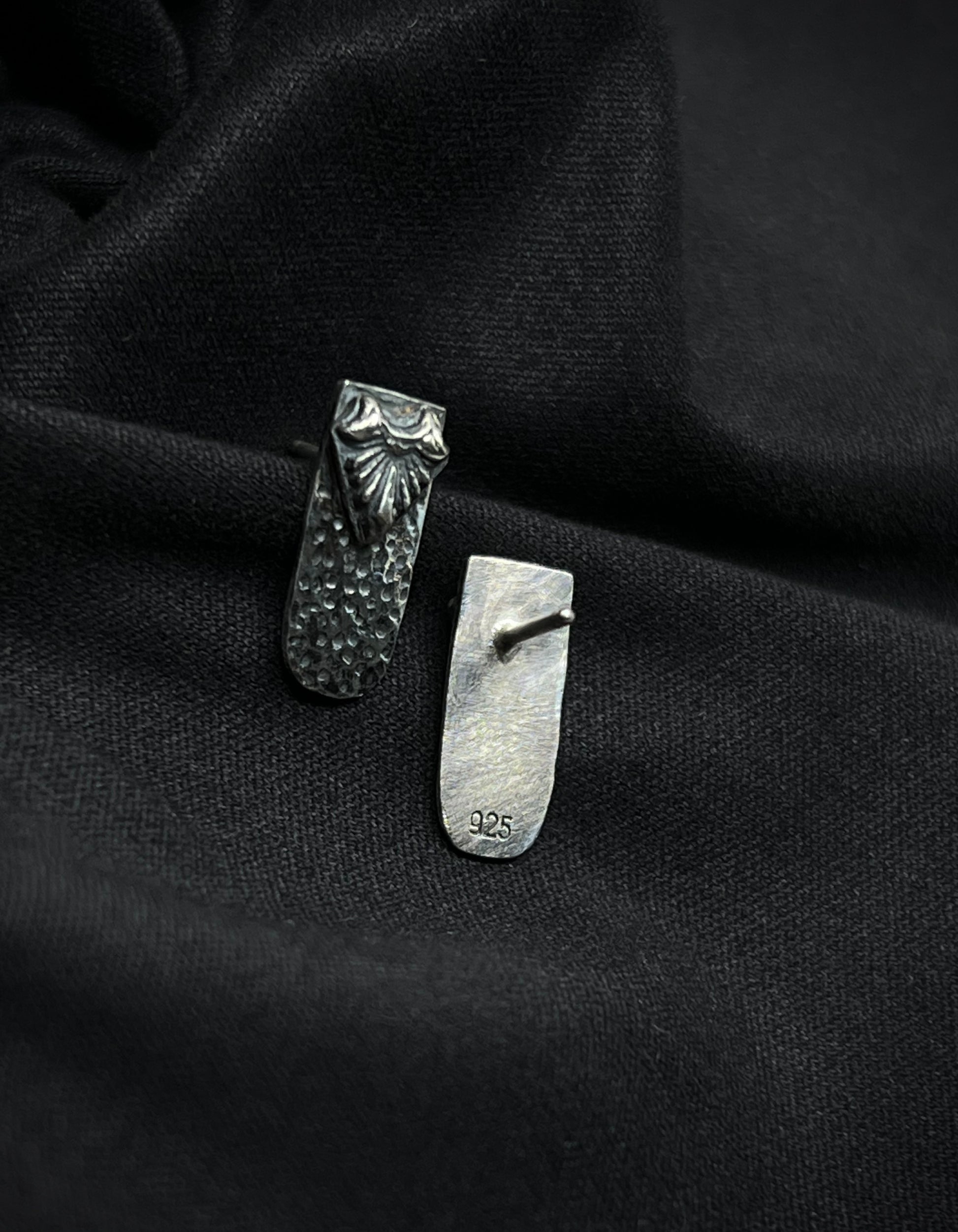Back and front view of Ashborn Root silver studs on black fabric, showing the 925 sterling silver hallmark and the high-contrast radiating design with hammered textures.