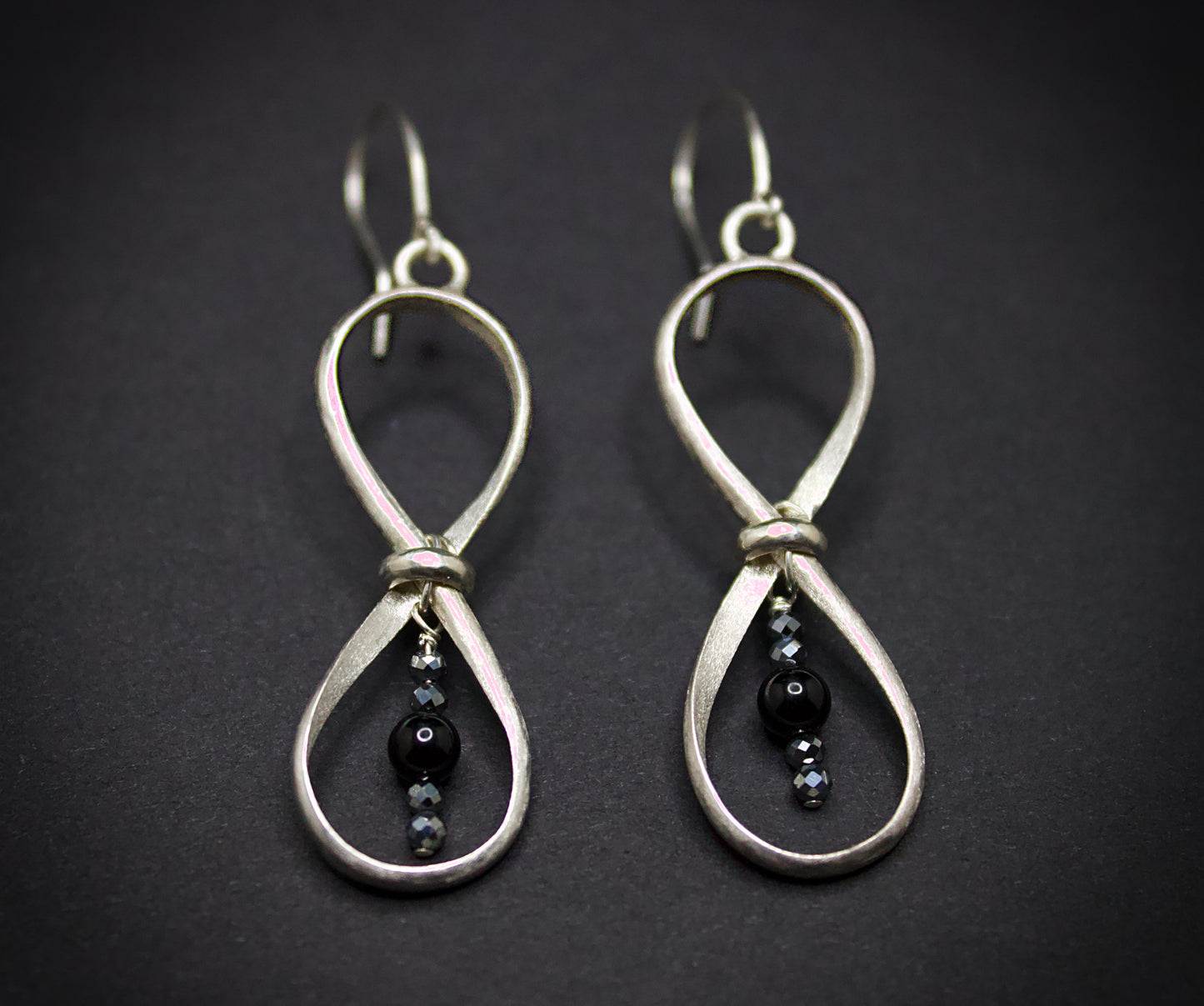 Silver earrings with black beads on a dark background