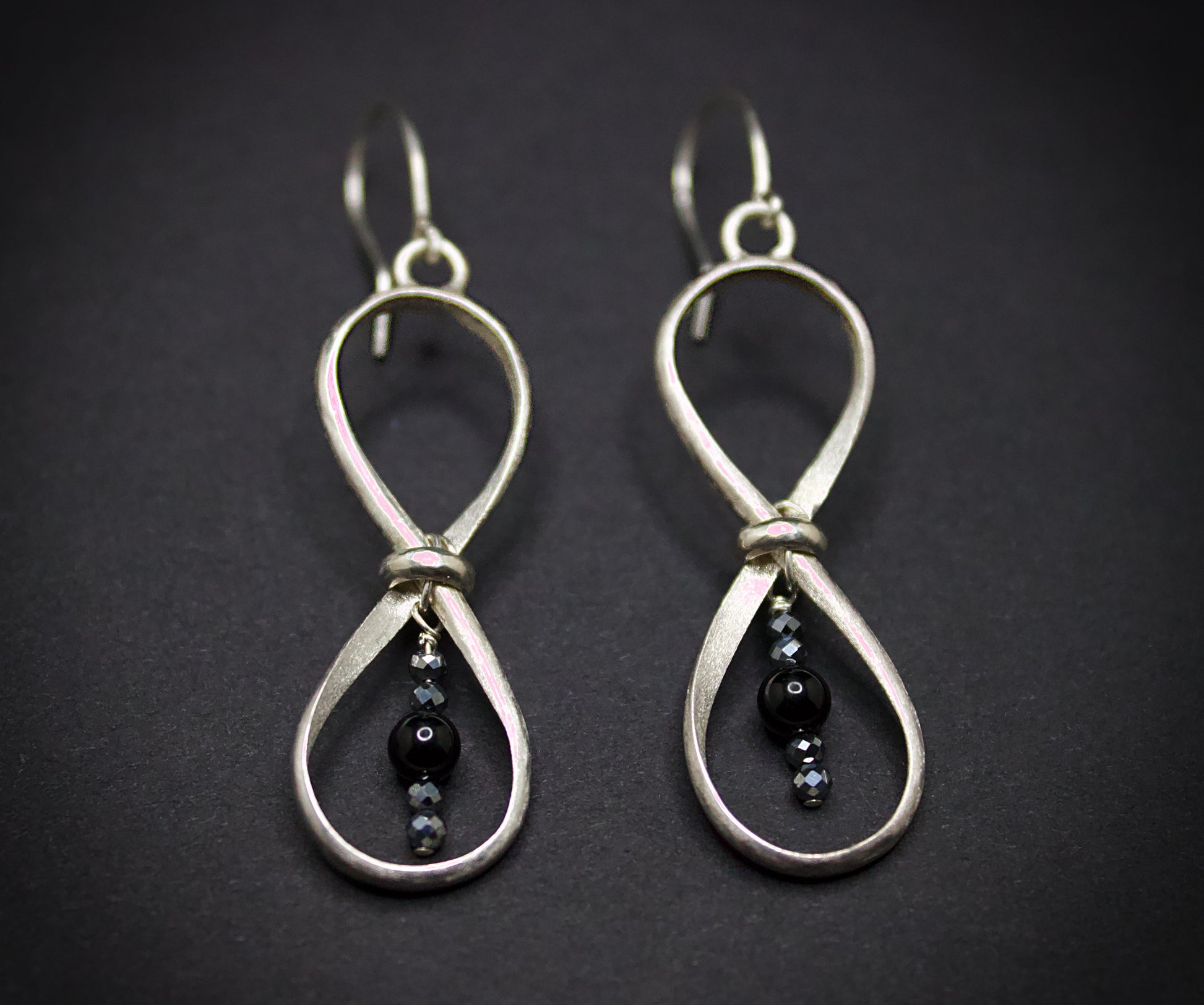 Silver earrings with black beads on a dark background
