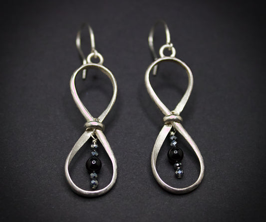 Silver earrings with black beads on a dark background