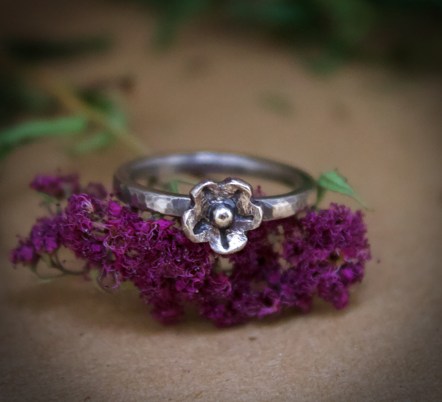 Silver ring with a floral design on purple flowers against a brown background