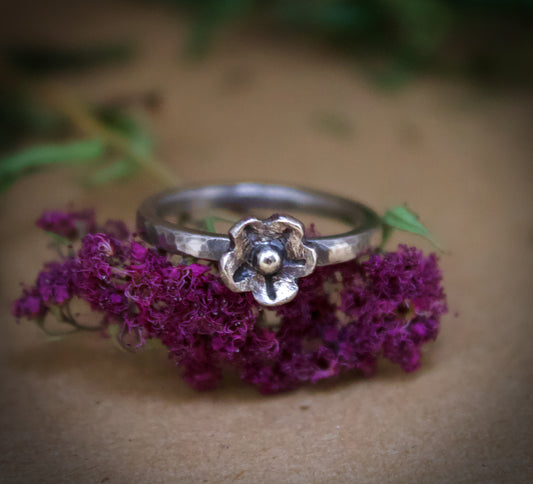 Silver ring with a floral design on purple flowers against a brown background