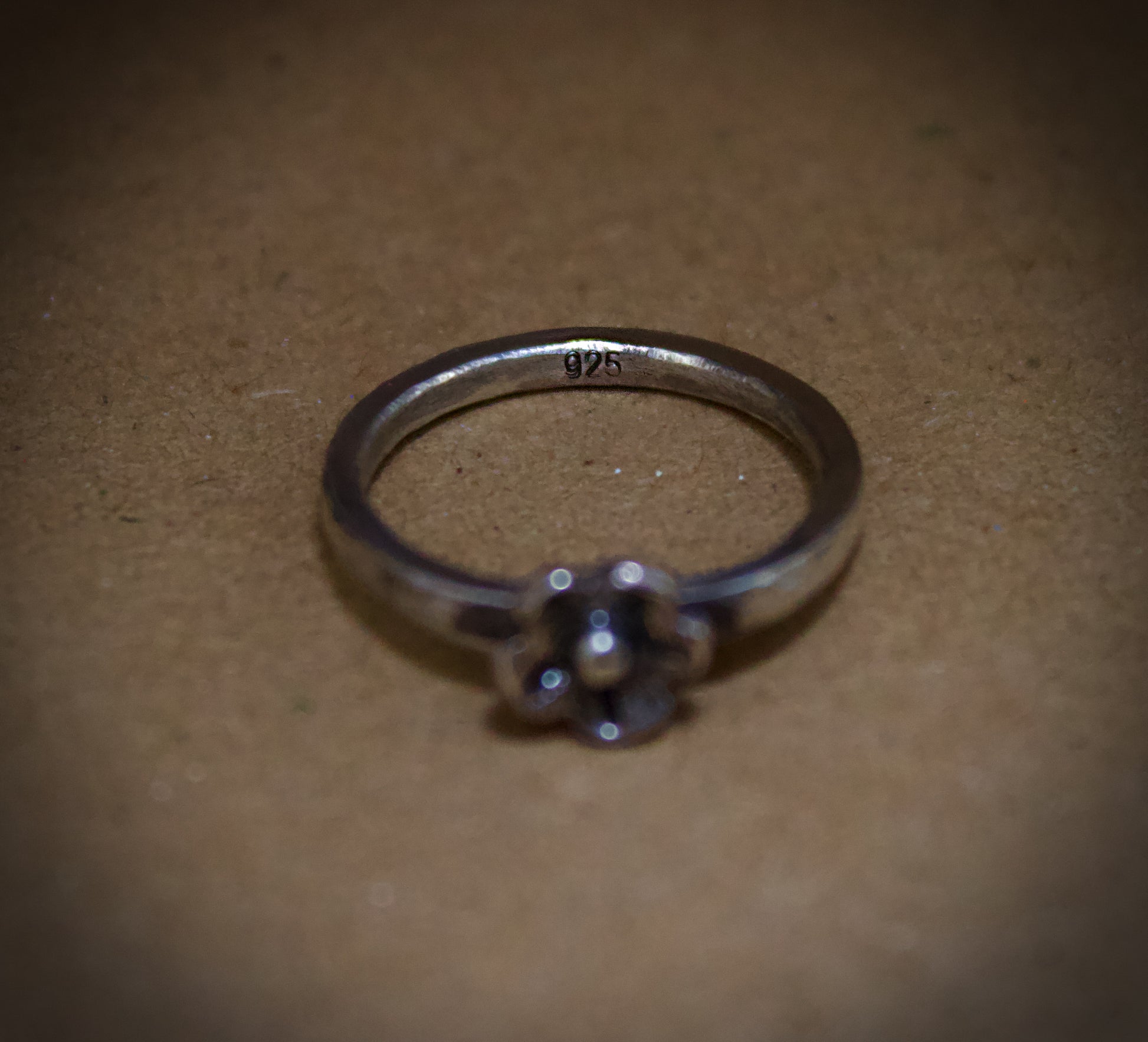 Silver ring with floral design on a brown surface showing it's "925" mark.