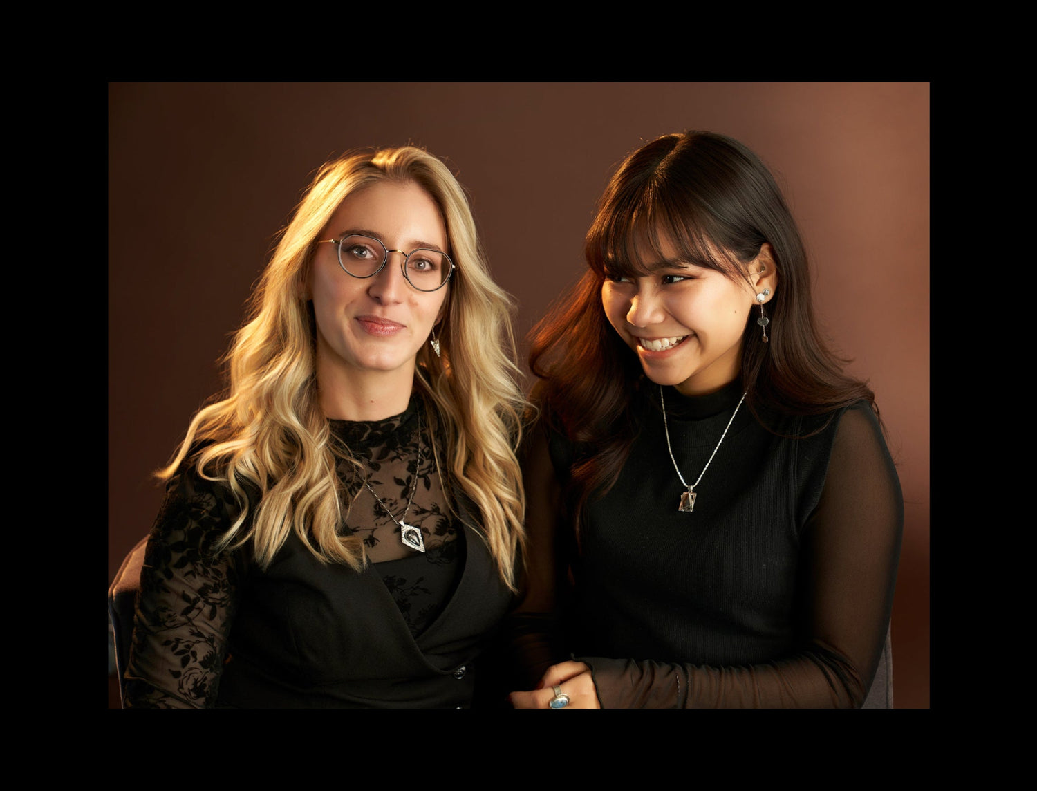 Two women posing together against a brown background