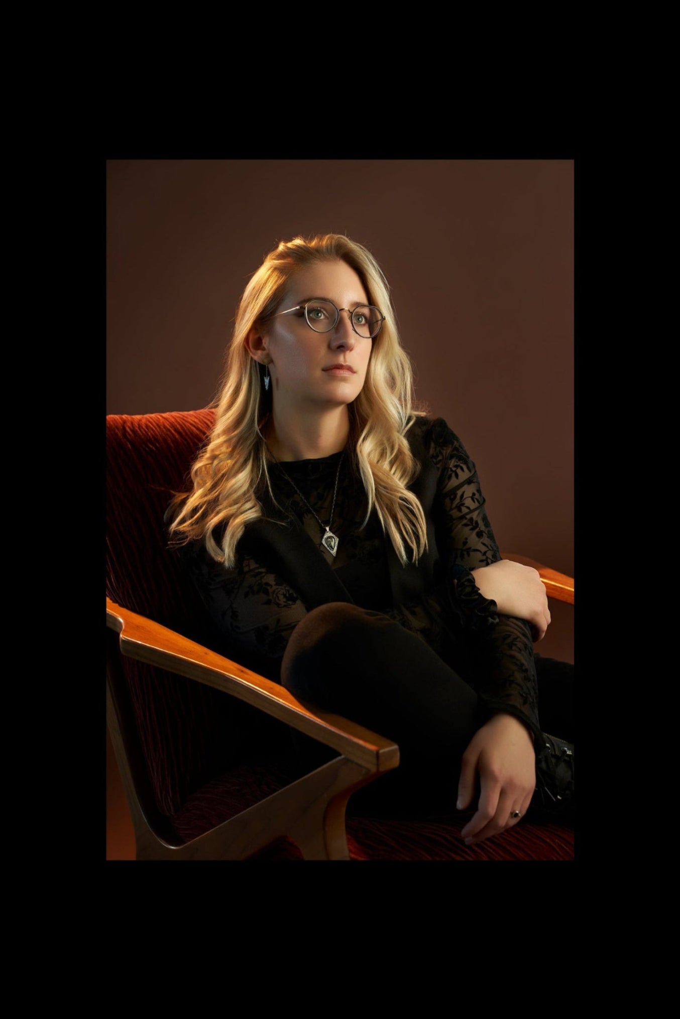 Woman with glasses sitting on a red chair against a brown background