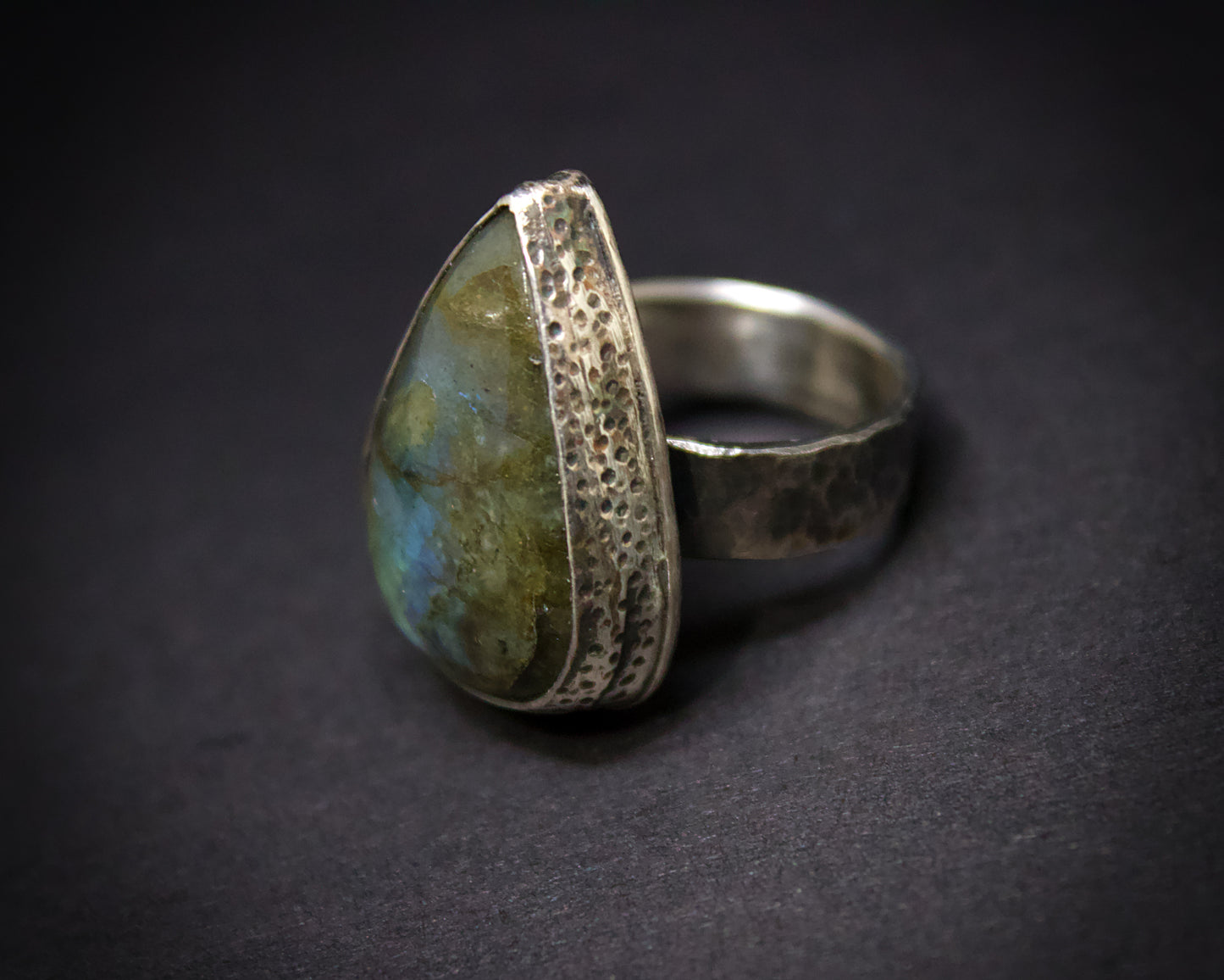 Silver ring with a textured band and stone on a dark background