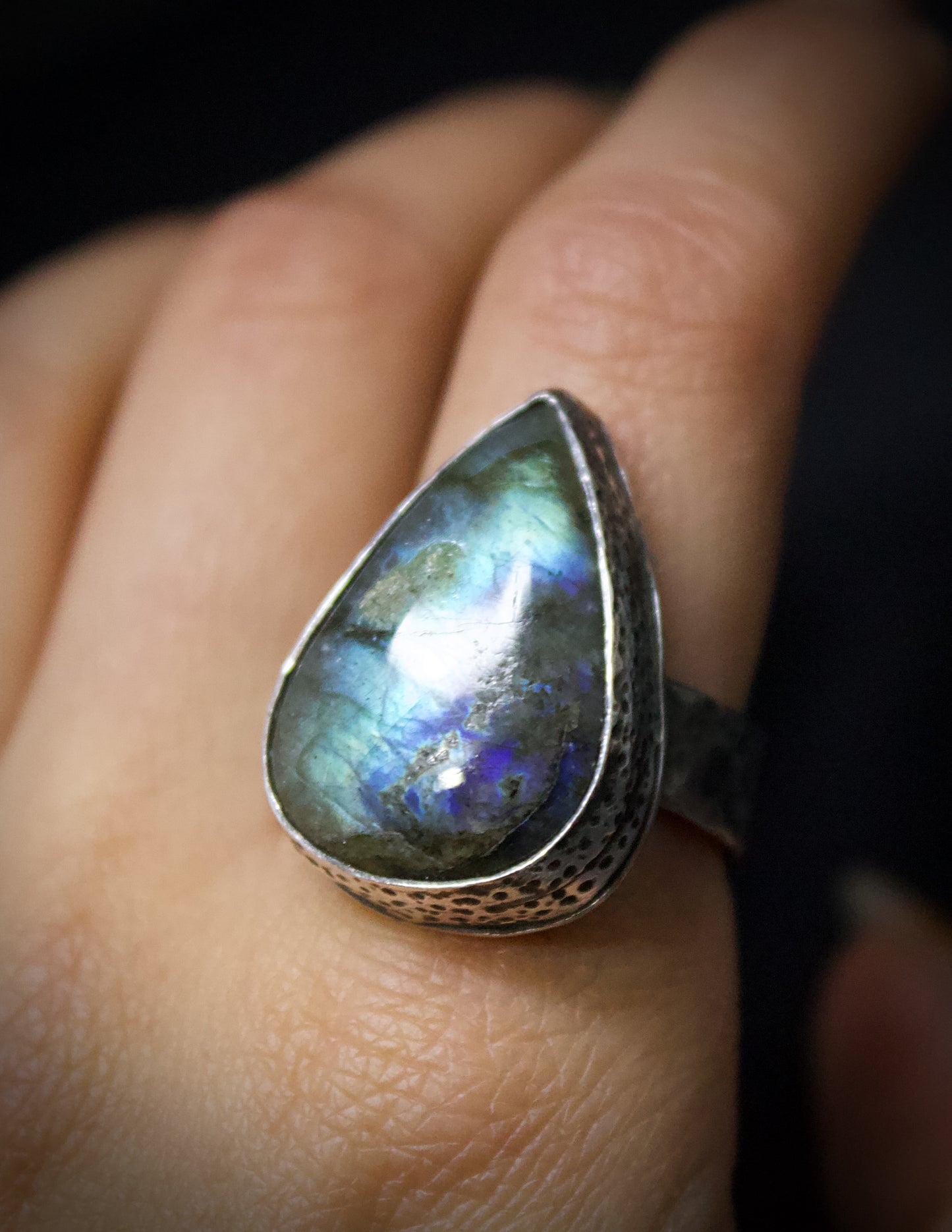 Teardrop-shaped gemstone ring on a finger with a dark background