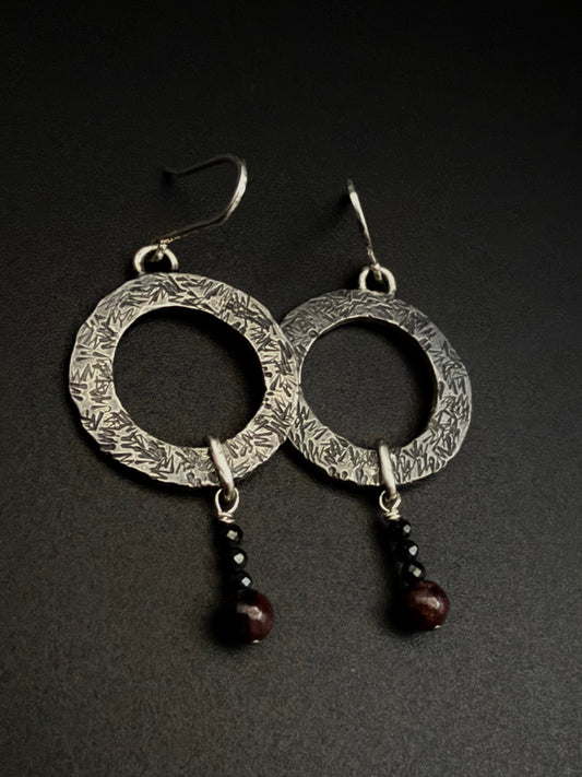 Silver hoop earrings with dark beads on a black background.