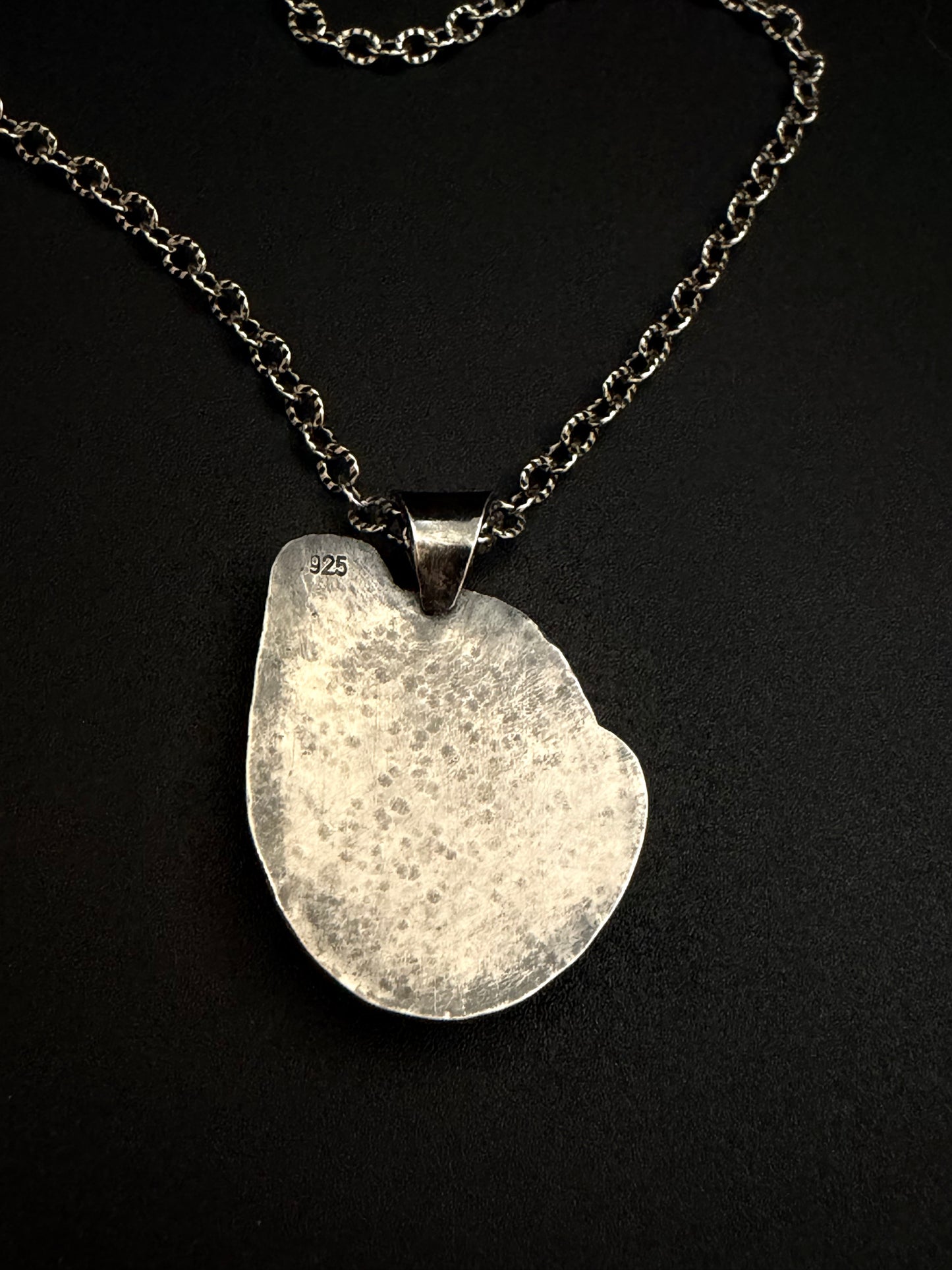 Silver necklace with a textured pendant on a black background