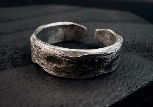 Silver ring with textured surface on a dark textured background