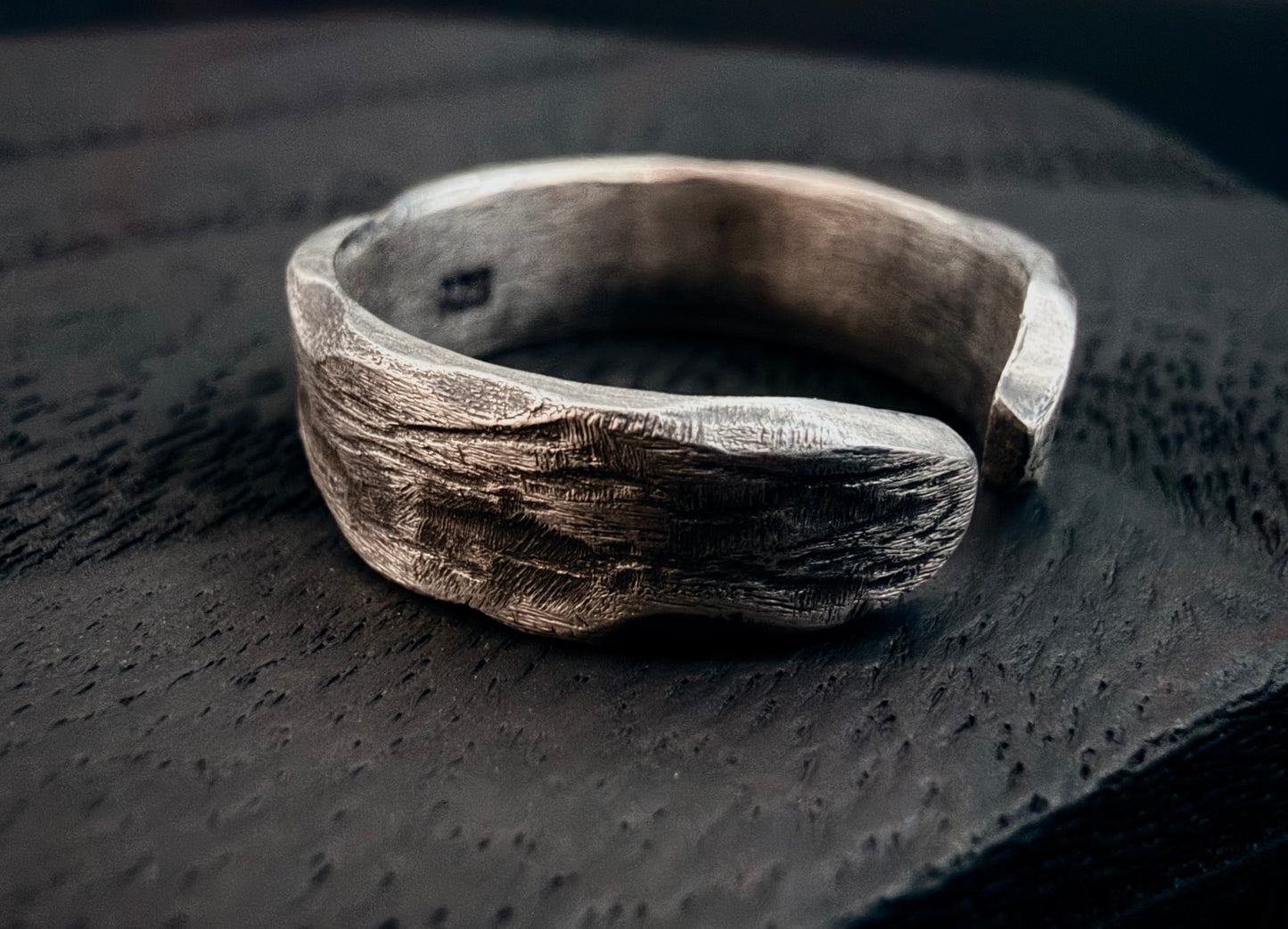 Silver ring with a textured surface on a dark textured background