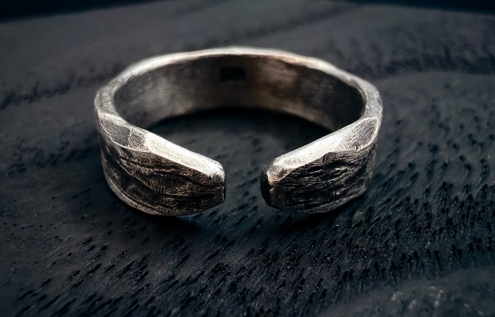 Silver ring with a textured design on a dark wooden surface