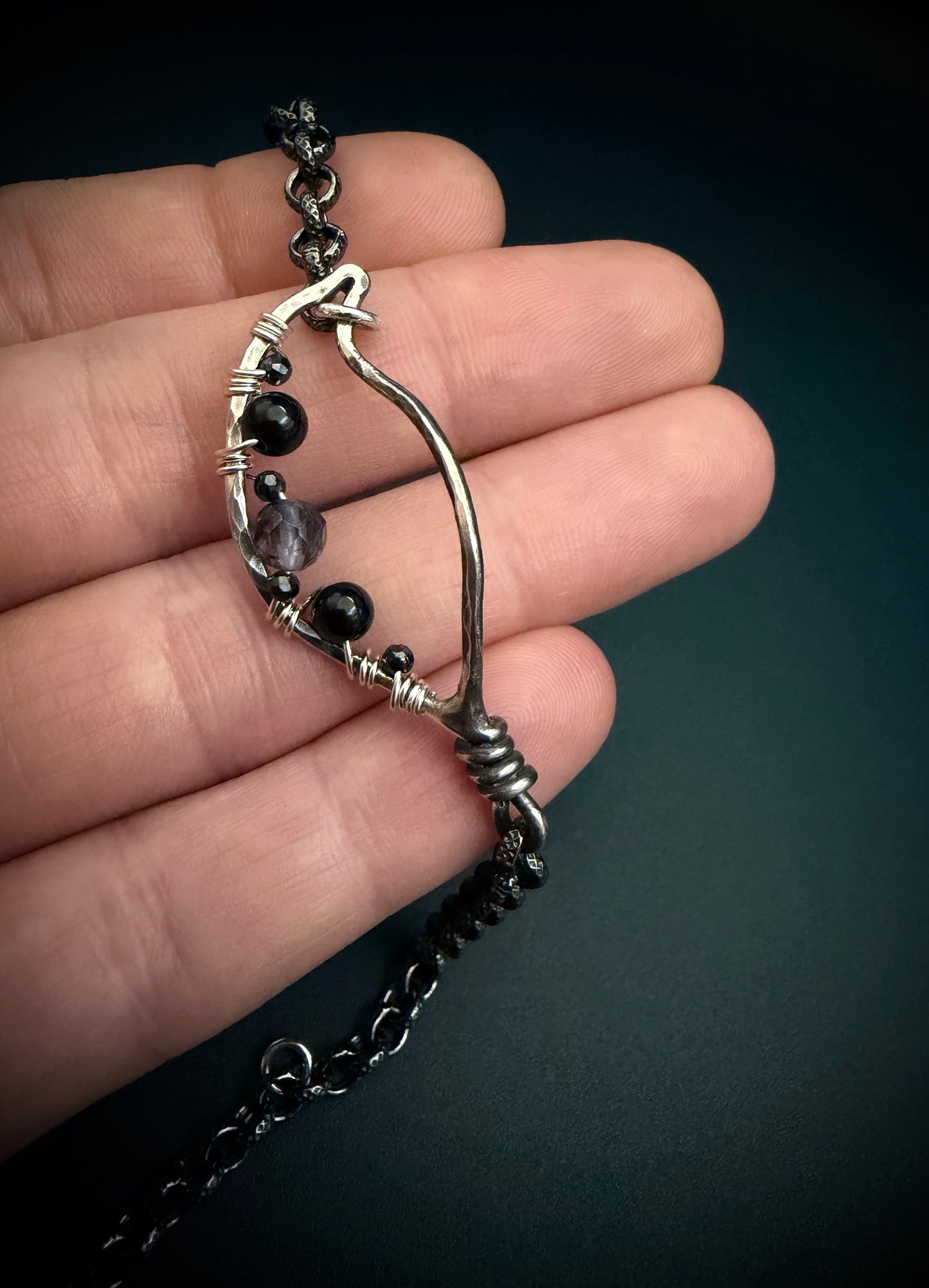 Silver leaf shape bracelet with stones held in a hand against a dark background