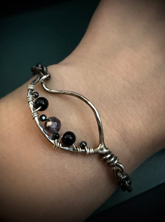 Silver bracelet with black beads on a wrist against a dark background