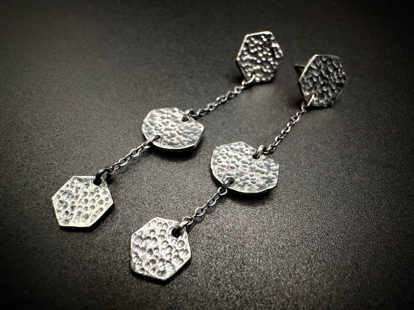 Silver earrings with textured hexagonal pendants on a dark surface
