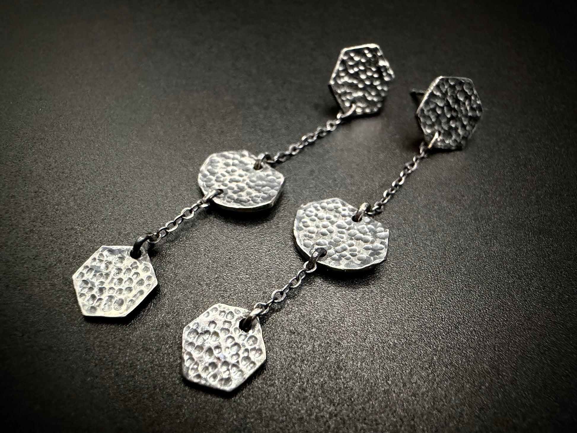 Silver earrings with textured hexagonal pendants on a dark surface