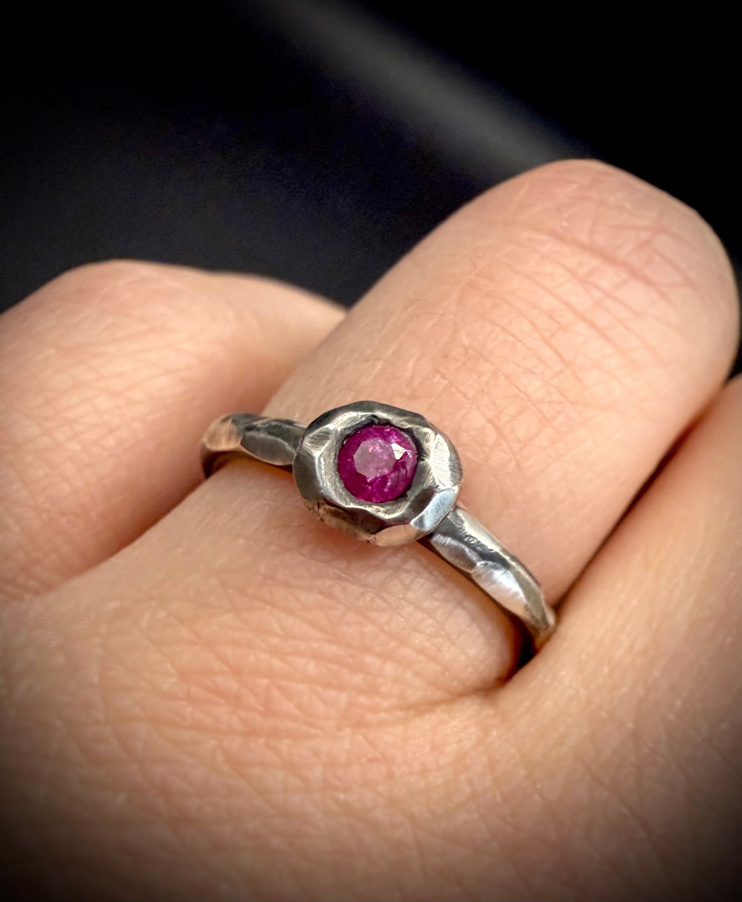 Silver ring with a pink gemstone on a finger against a dark background