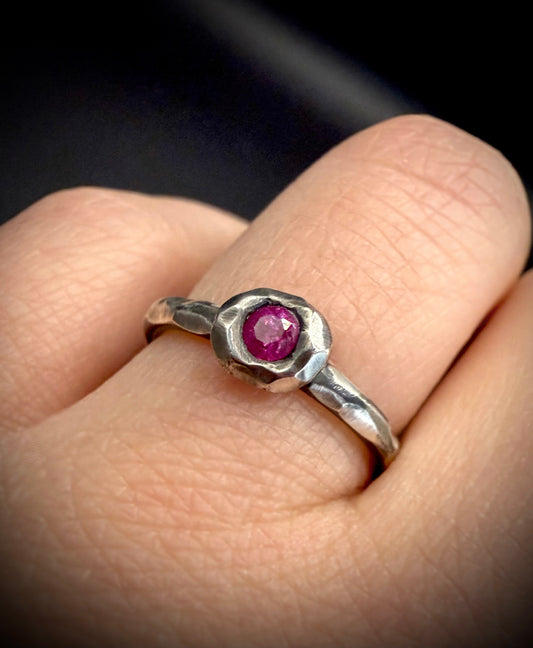 Silver ring with a pink gemstone on a finger against a dark background