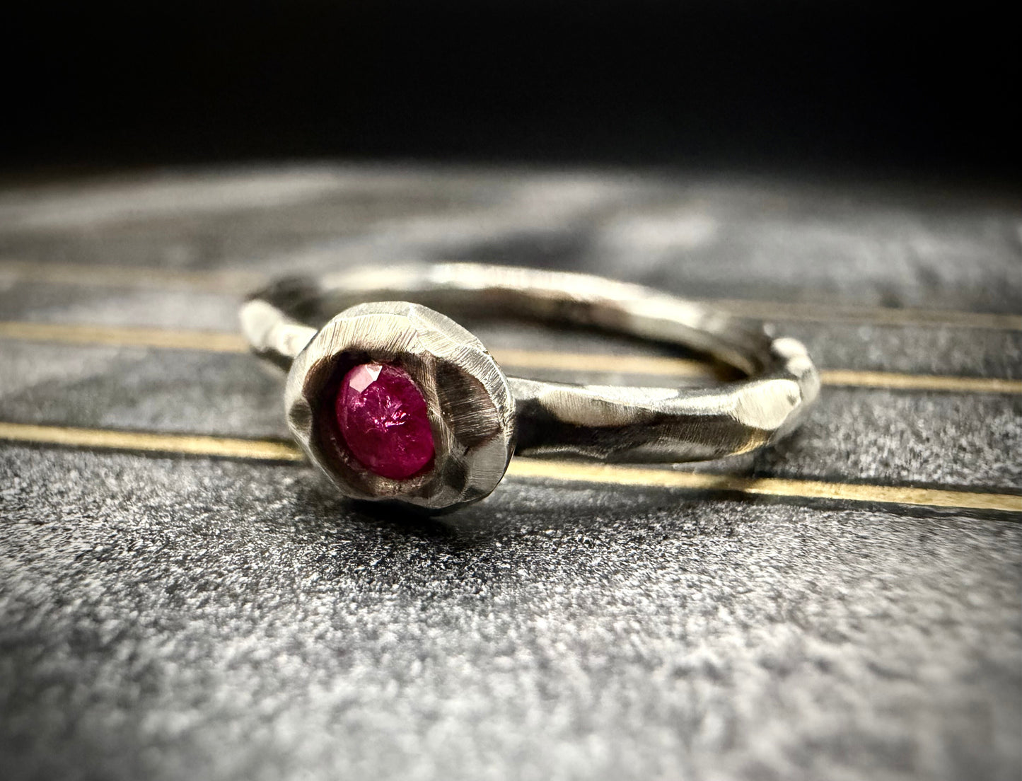Silver ring with a red gemstone on a textured surface