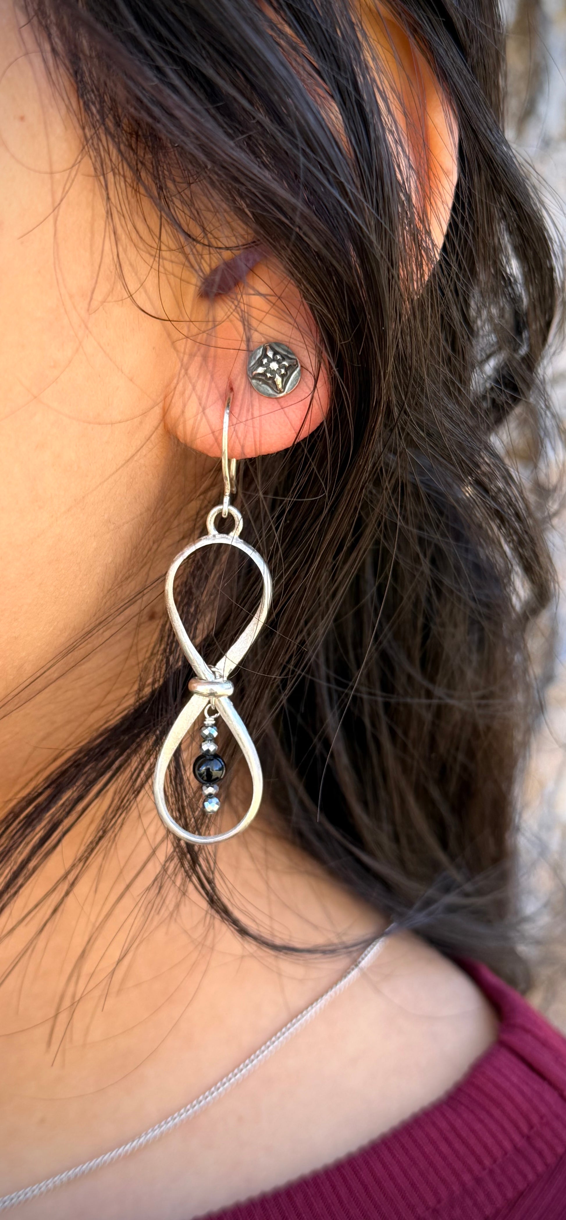 Close-up of a person wearing a silver infinity symbol earring with beads.