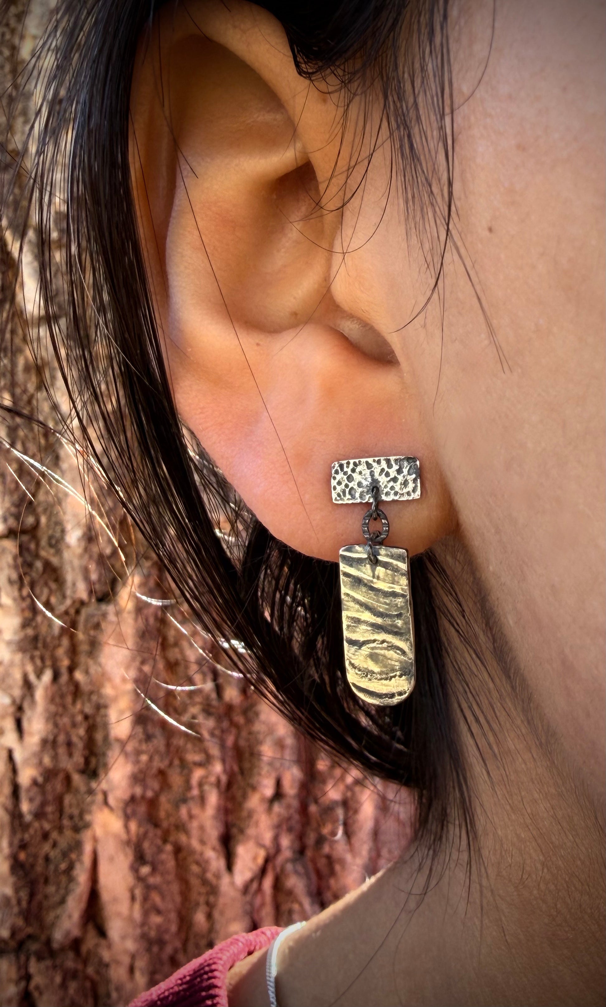 Close-up of an ear wearing a silver earring with a tree trunk background