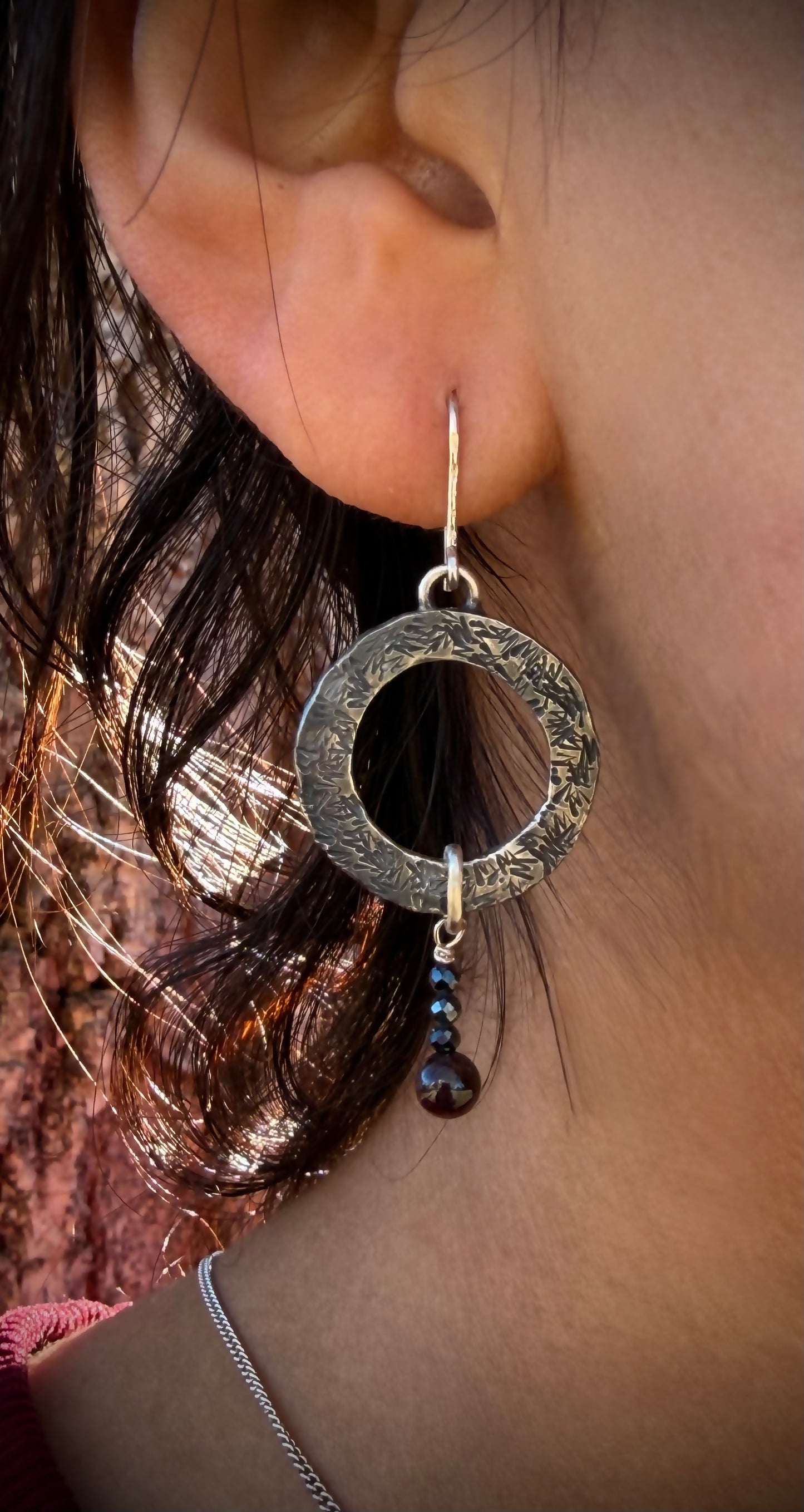 Close-up of an ear wearing a silver hoop earring with a dark bead.