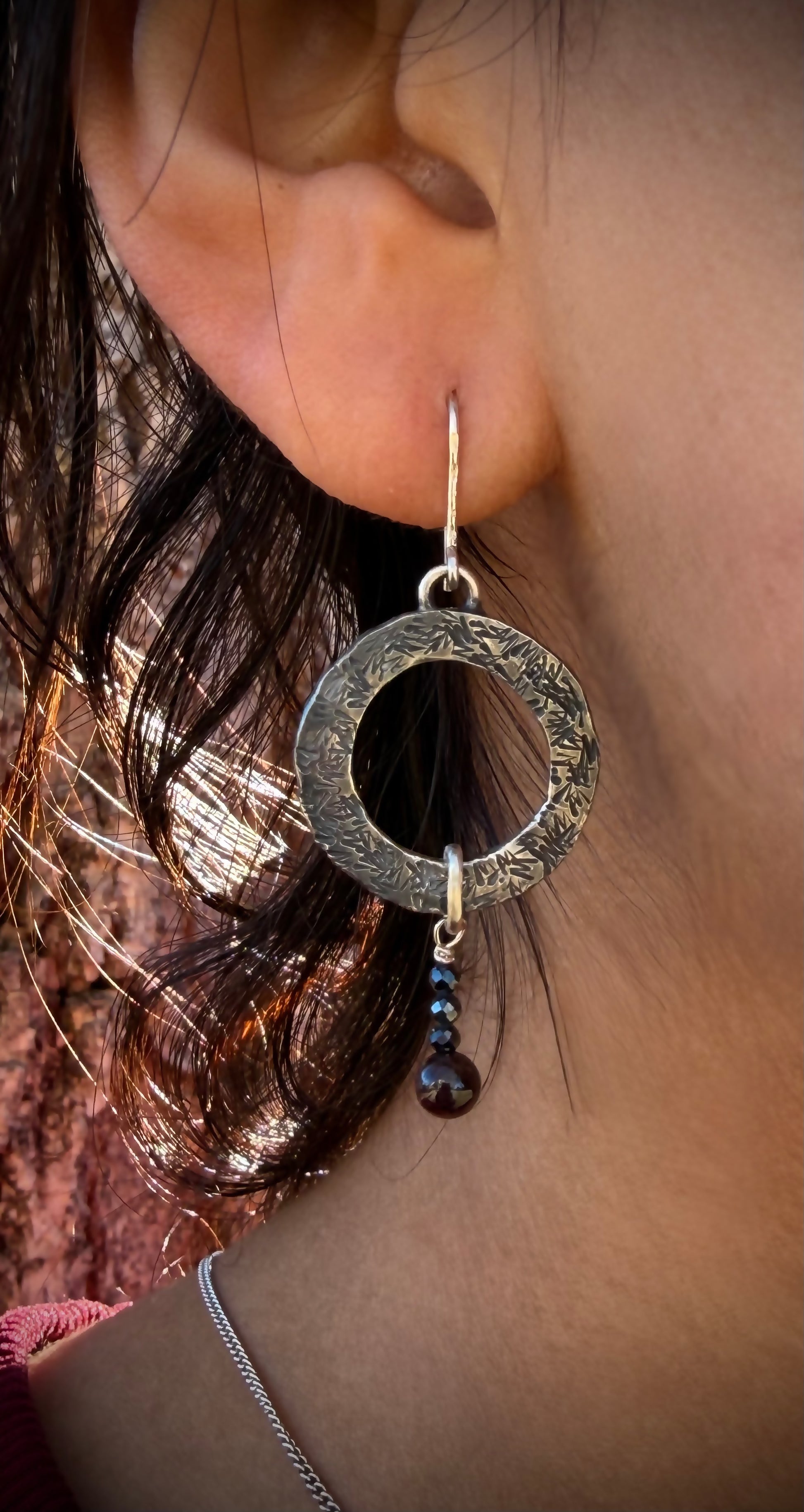 Close-up of an ear wearing a silver hoop earring with a dark bead.