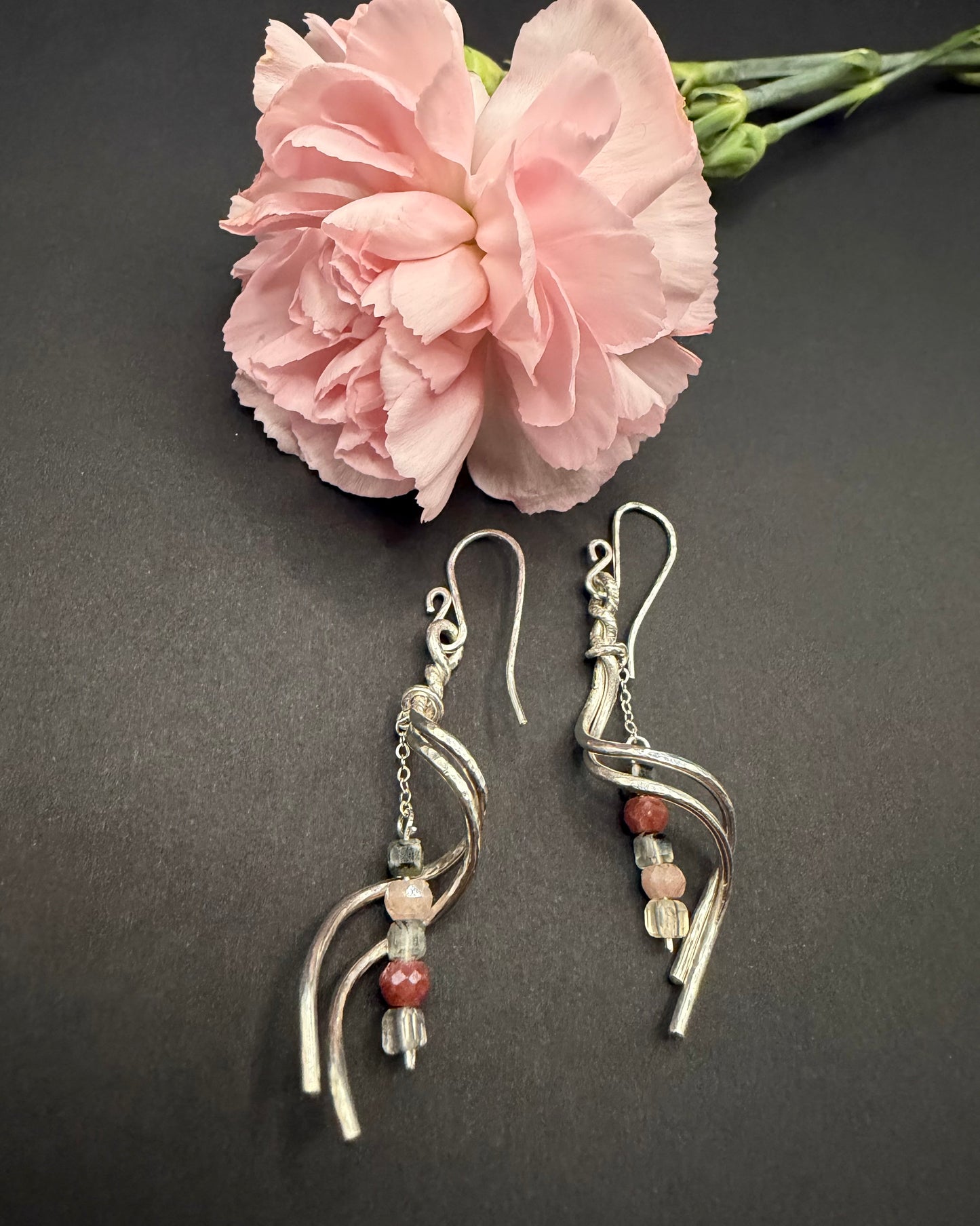 Detail view of silver Blushthorn earrings on a dark surface, showing the transition from a rough, textured 'thorn' top to a smooth polished dangle with Peach Moonstone and Prehnite beads.