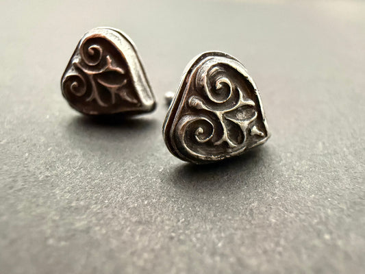 Pair of Ashborn sterling silver studs featuring a raised, triple-scroll design and dark patina, styled for a Dark Academia aesthetic on a textured gray background.