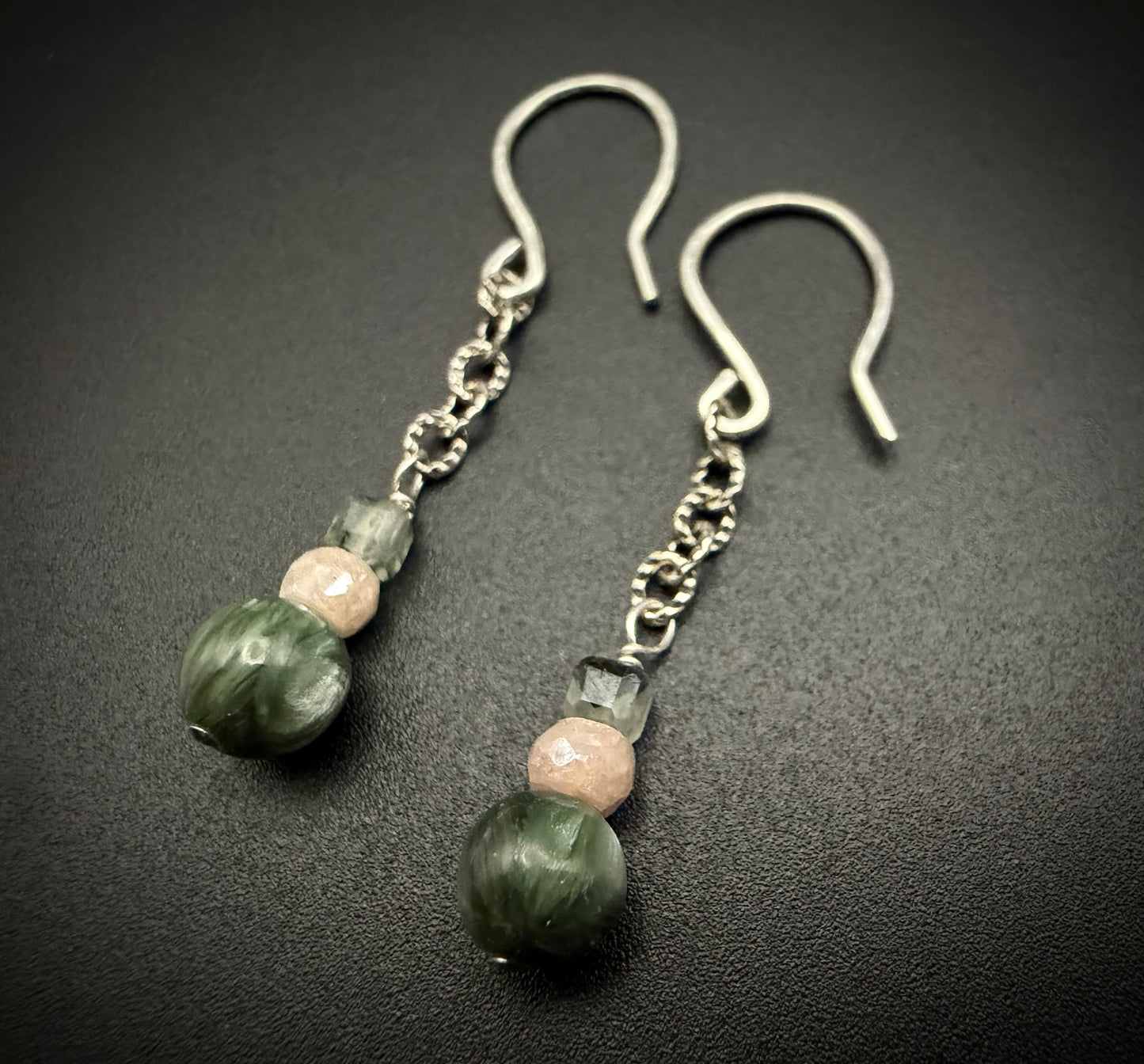 Handcrafted Lily Drops earrings featuring stacked beads of green Prehnite, peach moonstone, and dark green Seraphinite on sterling silver wires.